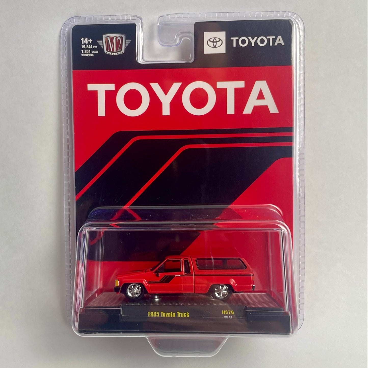 A packaged miniature die-cast model car of a 1981 Toyota truck, displayed in its original red and black blister card packaging on a neutral light gray background.