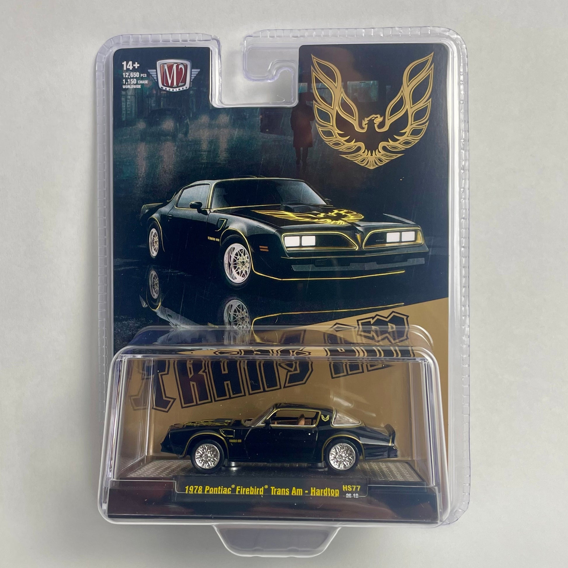 A packaged die-cast model car of a 1969 Pontiac Firebird 'Cosworth' Trans Am in black with gold accents, shown in its original blister pack against a light gray background.